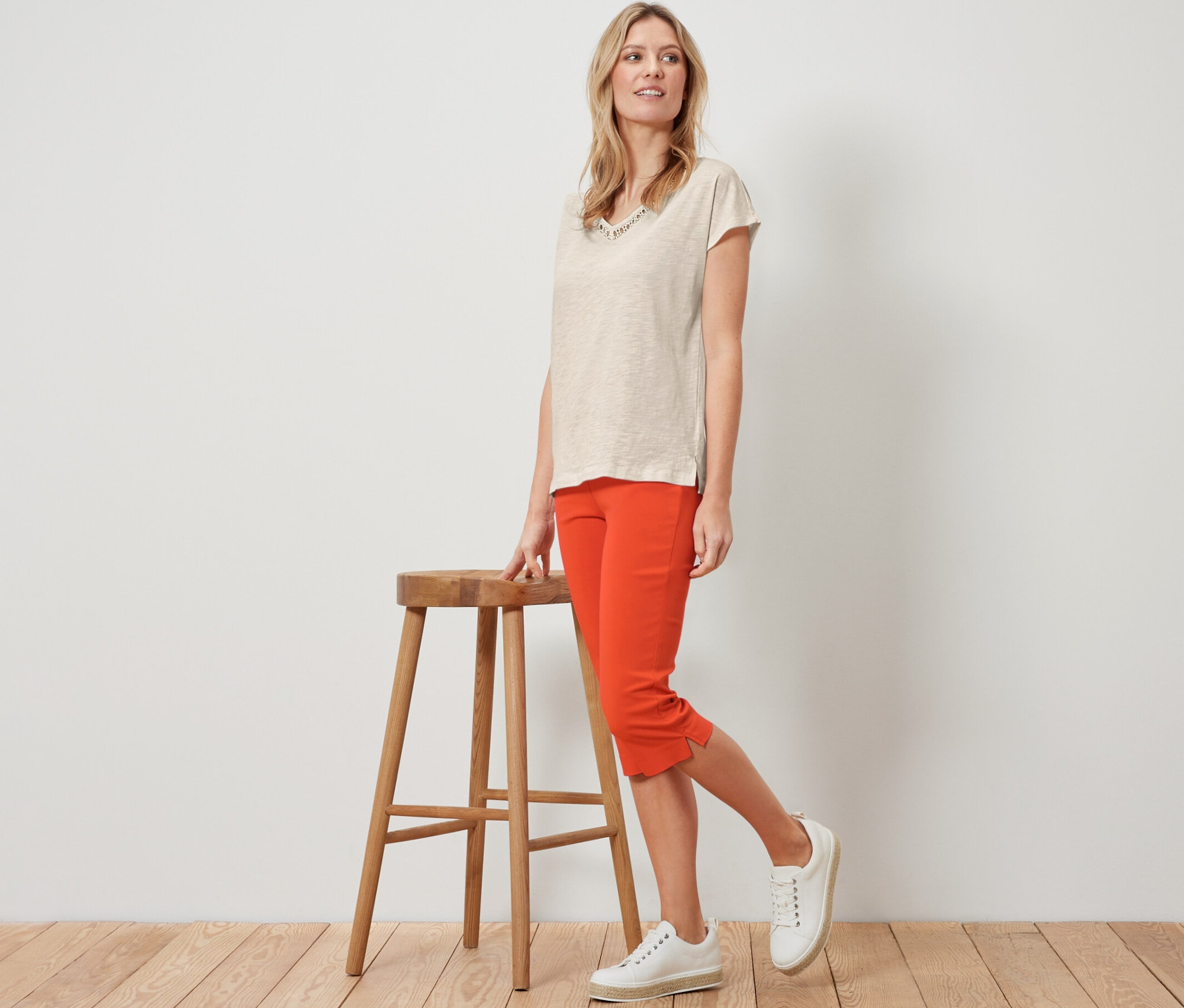 Blondínka pózuje vedľa drevenej stoličky v oranžových 3/4 elastických nohaviciach.