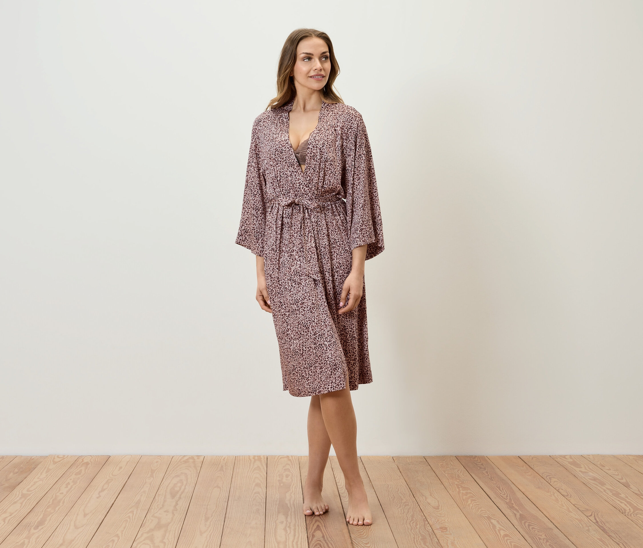 Žena stojí na drevenej podlahe a má na sebe župan s potlačou.