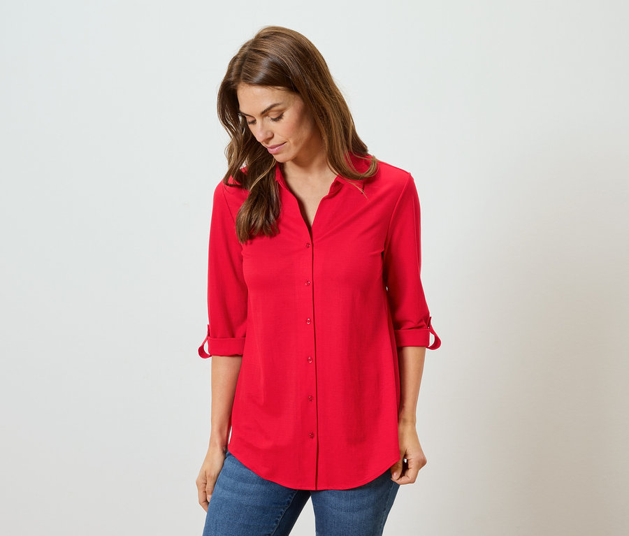 Žena má na sebe červenú košeľu a modré džínsy.