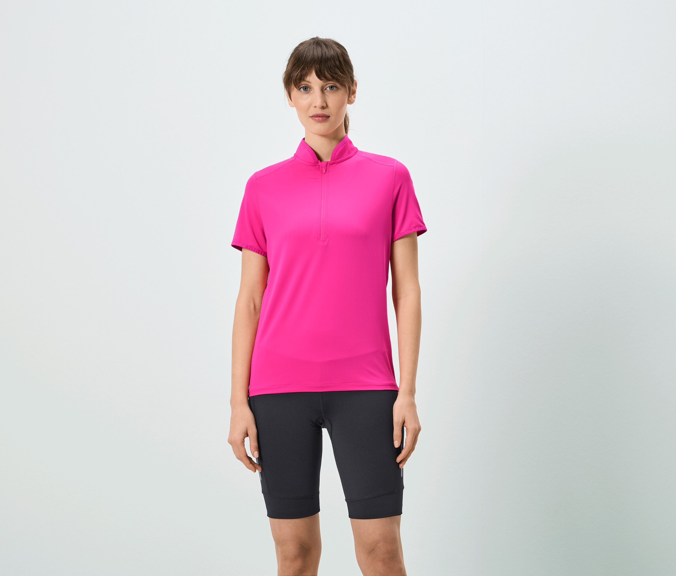 Žena má na sebe ružové tričko s krátkym zipsom a čierne šortky.