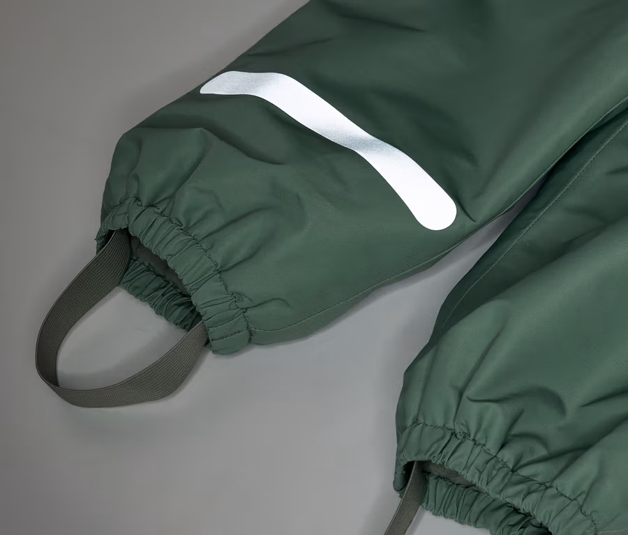 Detailný záber na zelené nohavice do dažďa s elastickými manžetami a reflexným pásikom na nohe.