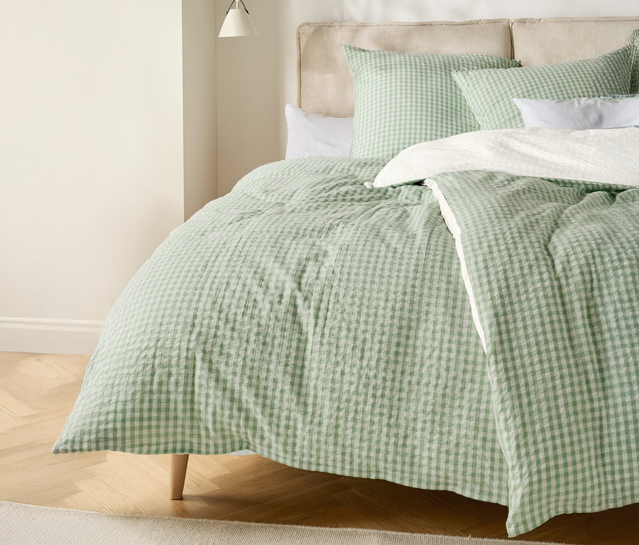 Posteľ s bledozelenou a bielou kockovanou prikrývkou a zodpovedajúcimi vankúšmi.