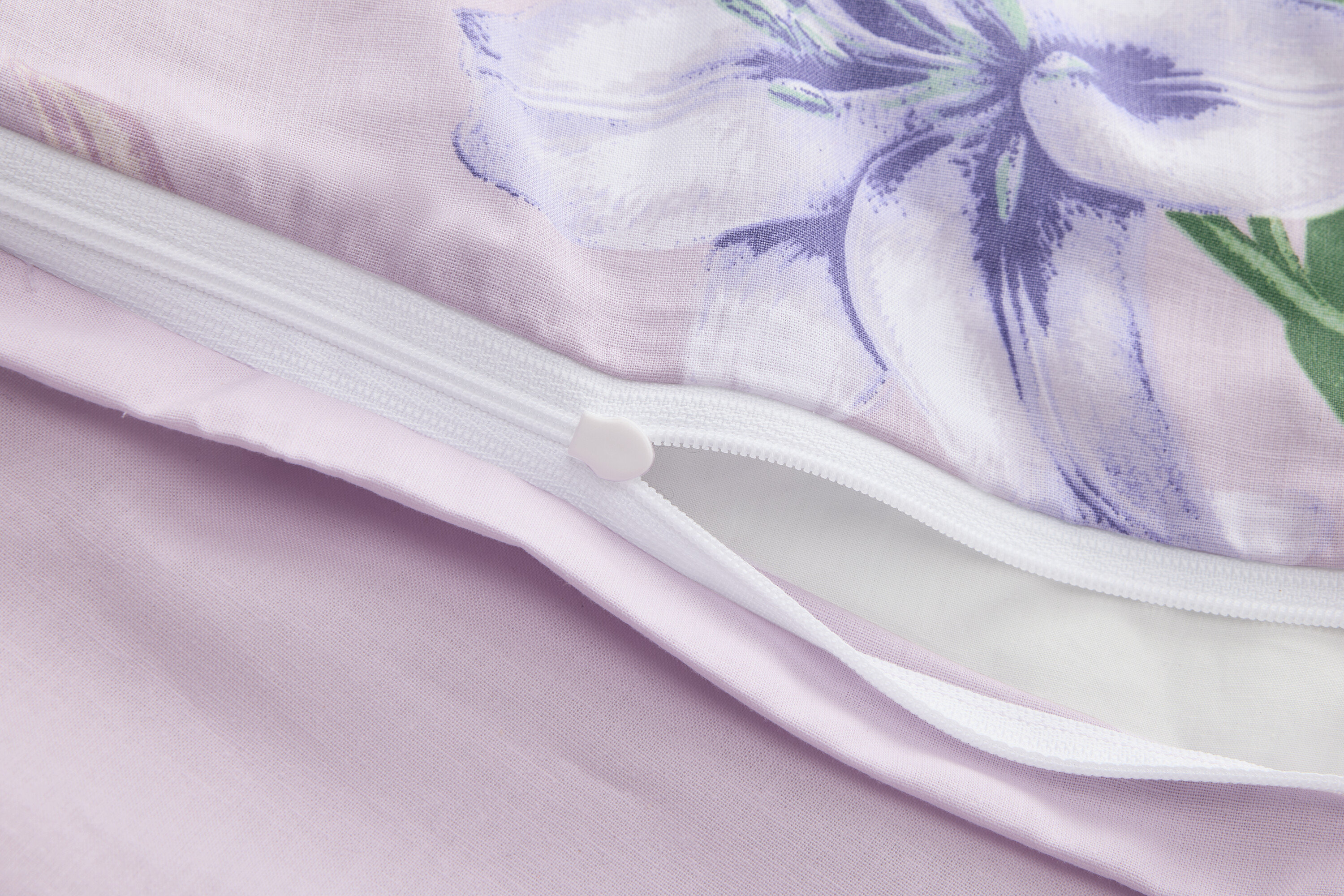 Detailný záber na čiastočne otvorenú fialovú obliečku na prikrývku s kvetinovou potlačou a zipsom.