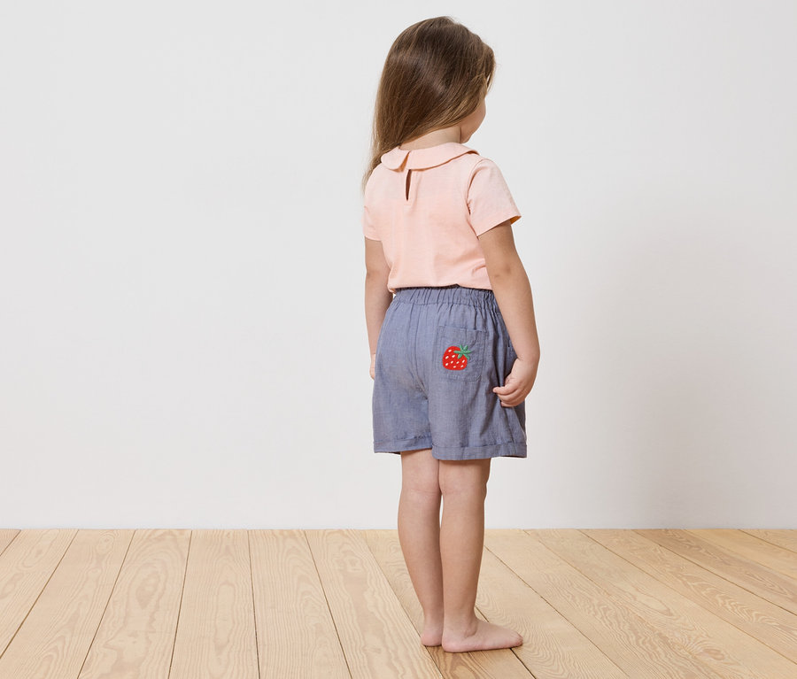 Dievča zozadu, má na sebe ružovú košeľu a modré šortky s jahodovou aplikáciou.