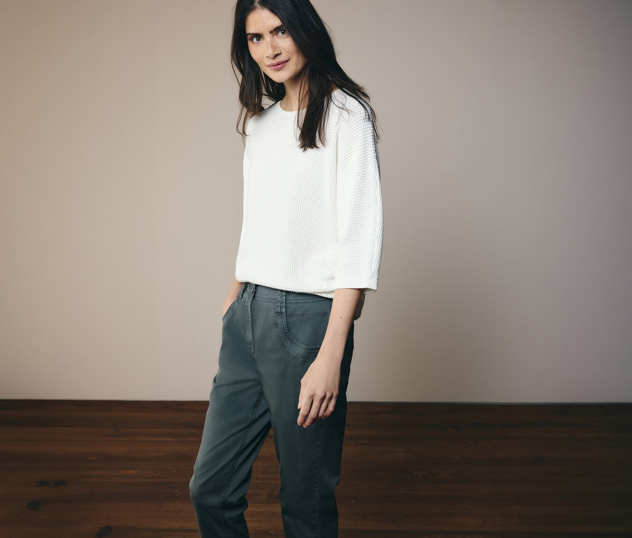 Žena v bielom tope a nohaviciach CECIL »Scarlett« v tmavozelenej farbe pózuje na svetlom pozadí.