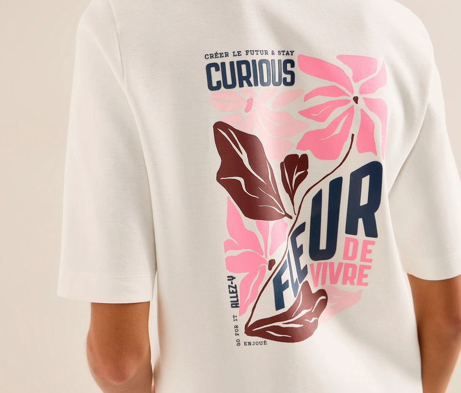 Osoba zozadu v bielej mikine CECIL s farebnou grafickou potlačou na chrbte. Potlač zobrazuje ružové kvety, hnedé listy a texty ako „CRÉER LE FUTUR & STAY CURIOUS“ a „FLEUR DE VIVRE“.