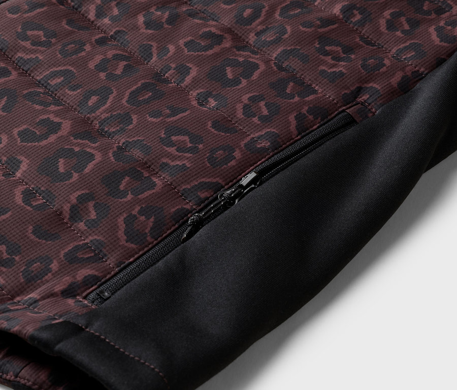 Detail záberu prešívanej bundy s leopardím vzorom a čiastočne otvoreným zipsom na boku.