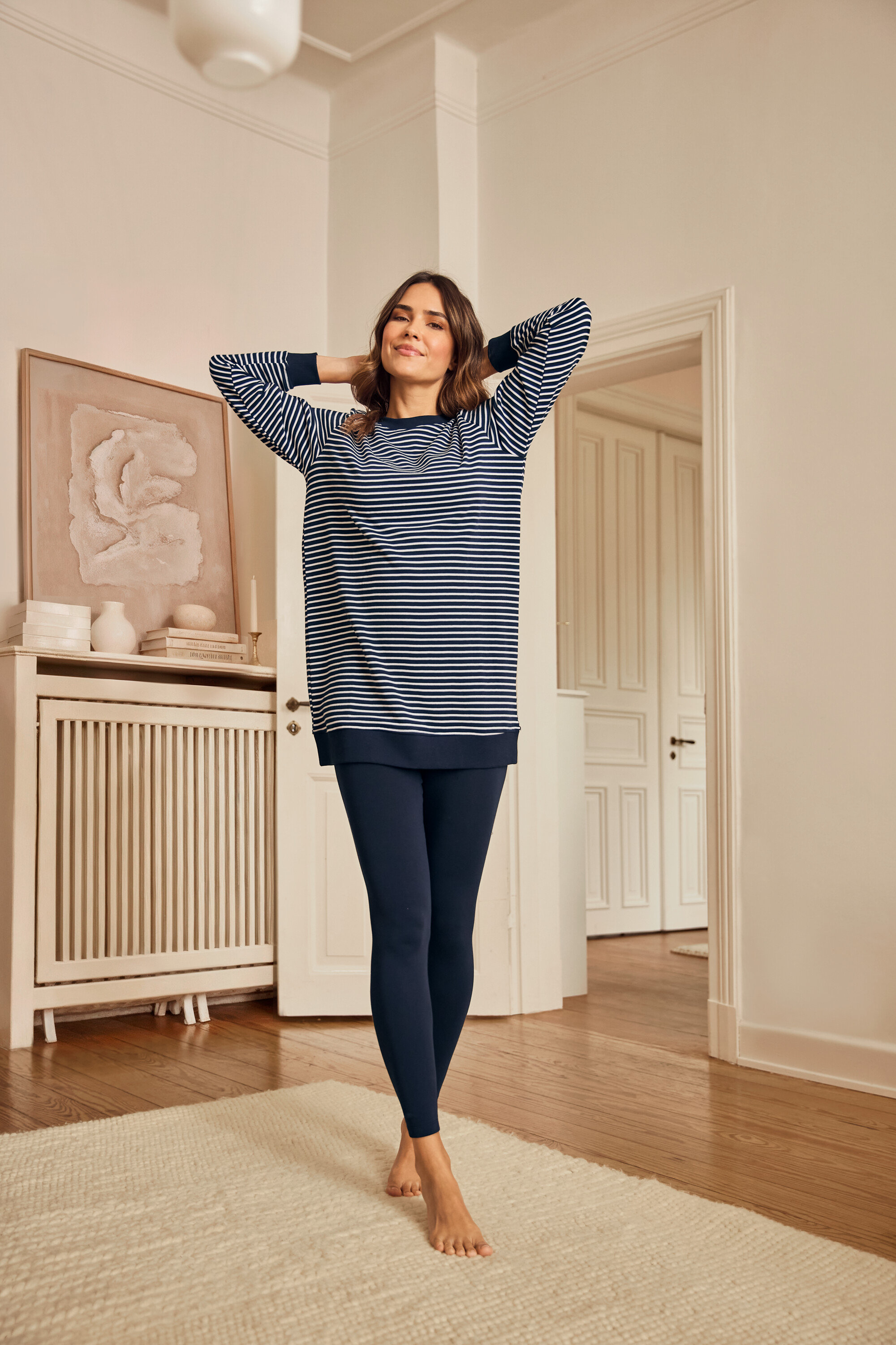 Žena v pyžame s legínami stojí naboso na koberci.