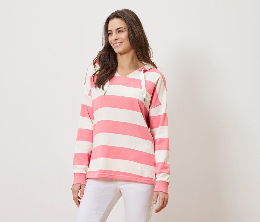 Žena má na sebe ružovo-bielu pruhovanú mikinu s kapucňou a biele nohavice.