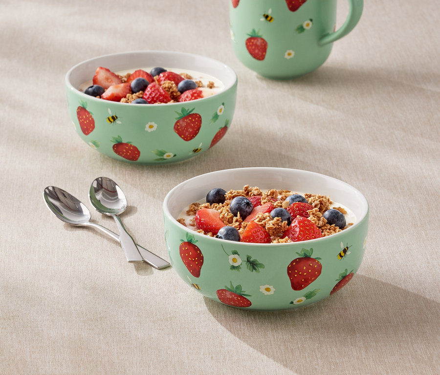 Dve misky naplnené jogurtom, jahodami a čučoriedkami so vzorom jahôd a džbán stoja na stole.