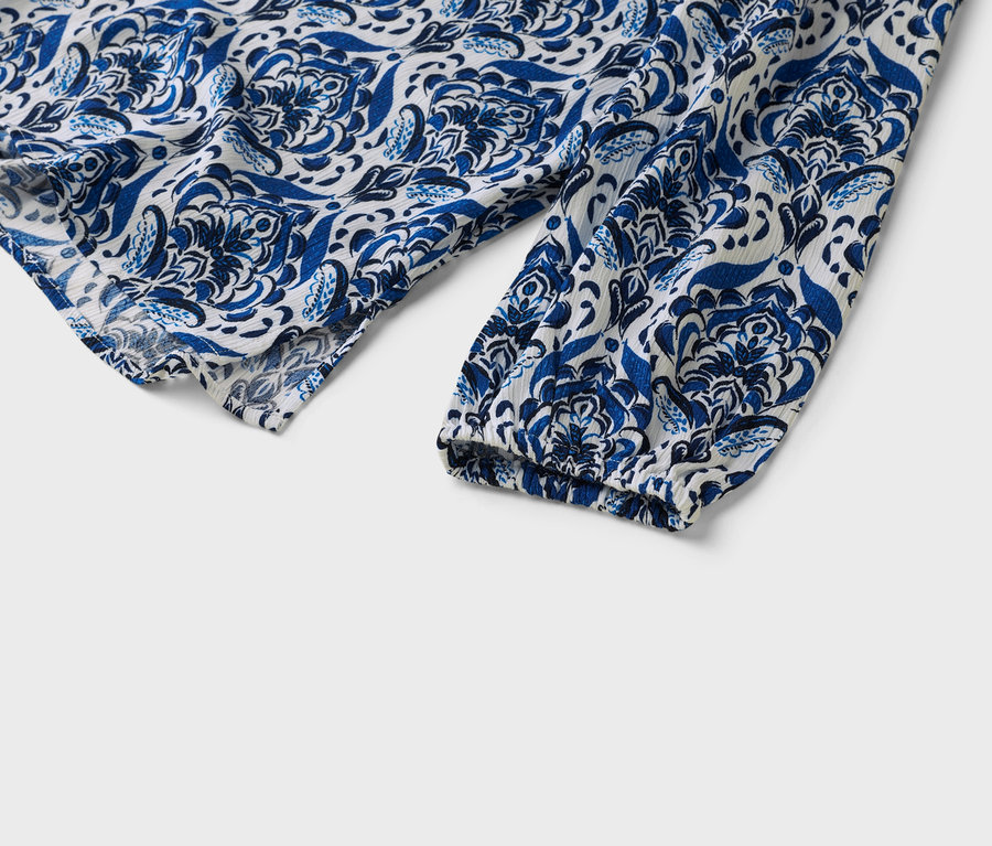 Detail záberu na bielo-modrý vzorovaný rukáv blúzky.