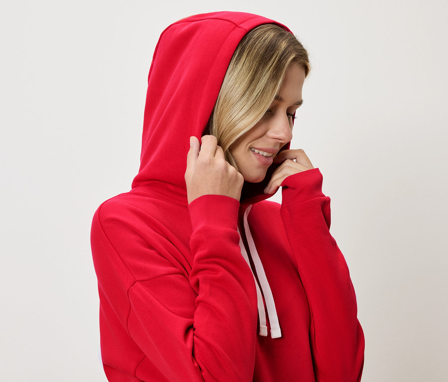Žena s blond vlasmi má na sebe červenú mikinu s kapucňou a drží kapucňu.