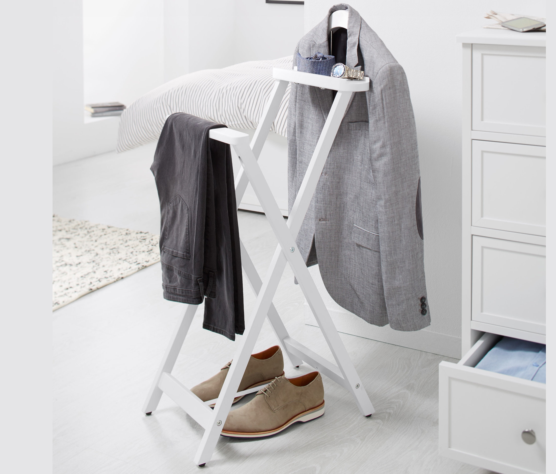 Na bielom pozadí stojí nemý sluha, na ktorom visí sivé sako a nohavice, pod ním stoja hnedé topánky.