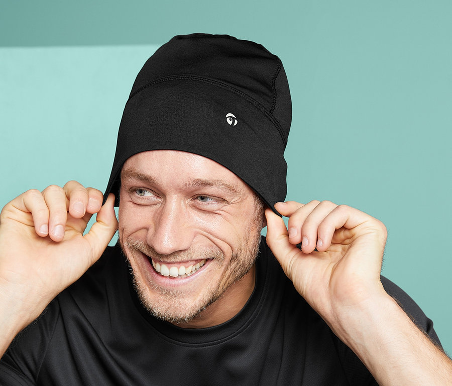Muž sa usmieva a drží okraje svojej čiernej funkčnej čiapky, unisex.