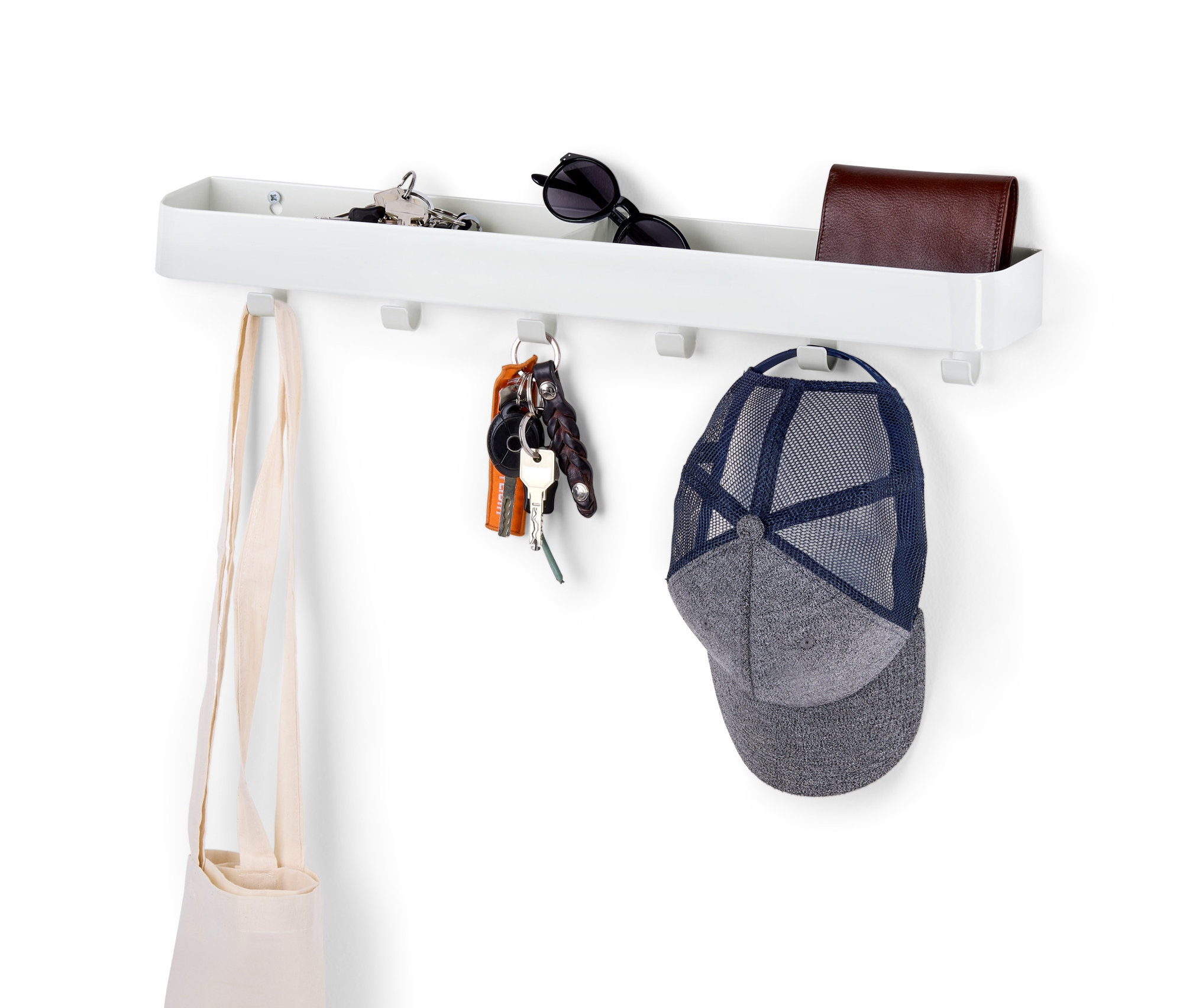 Biela polička na kľúče s odkladacou plochou na bielej stene s kľúčmi, taškou, peňaženkou a šiltovkou.