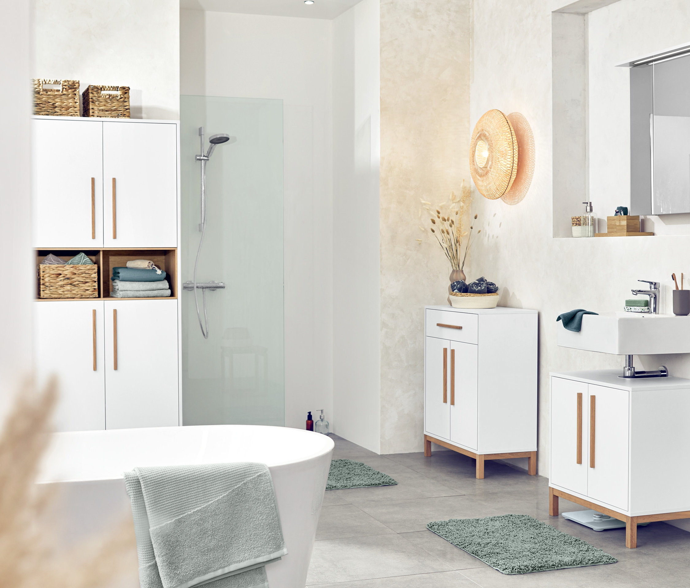 Interiér kúpeľne s bielym nábytkom, vrátane vysokej skrinky Eklund, skrinky pod umývadlo a odkladacej skrinky, 2 ks úložných košíkov, stropného svietidla a predložiek do kúpeľne 70x120 cm a 50x80 cm.