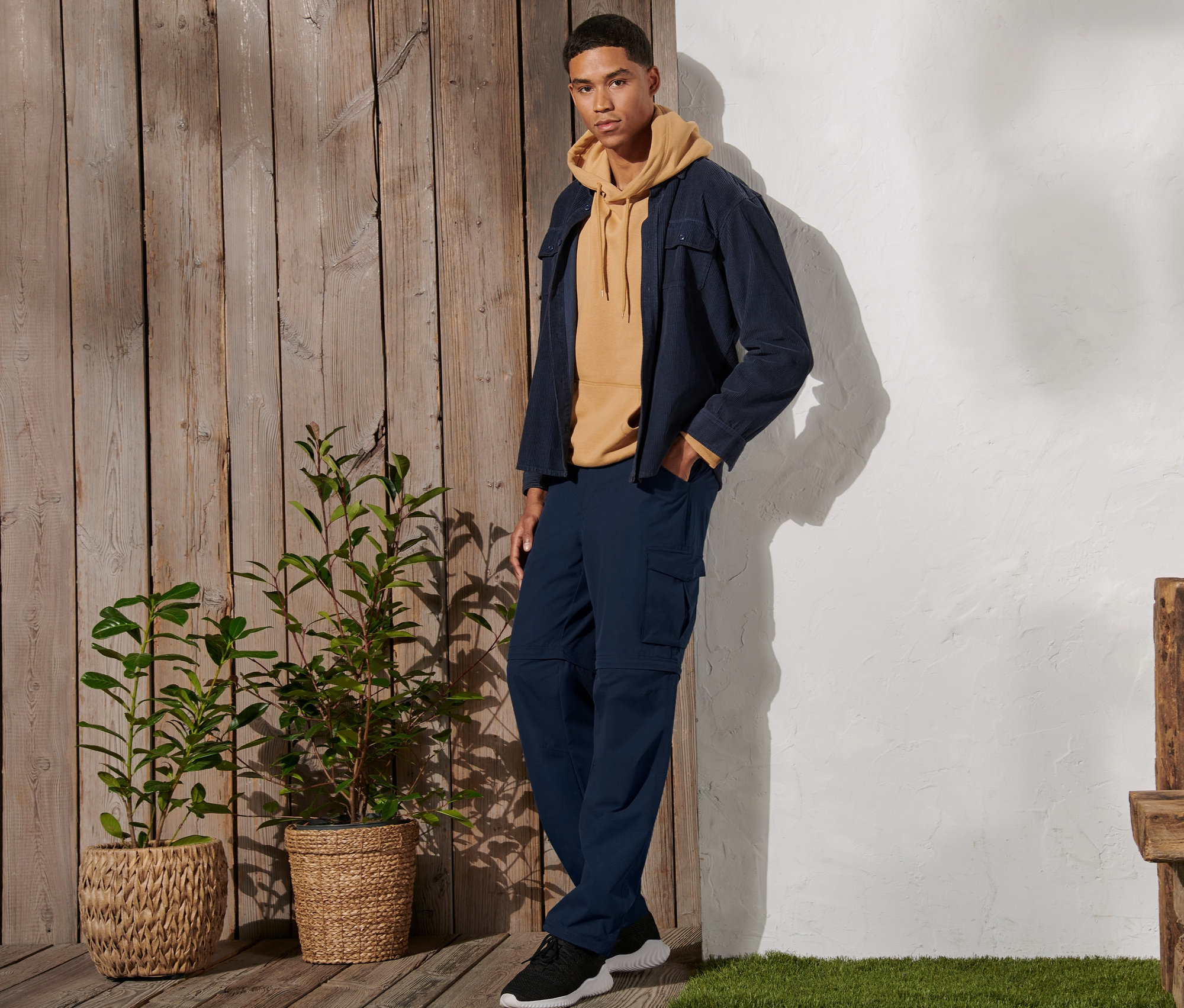 Muž stojí a má na sebe tmavomodré funkčné nohavice 2 v 1, žltú mikinu a bundu.
