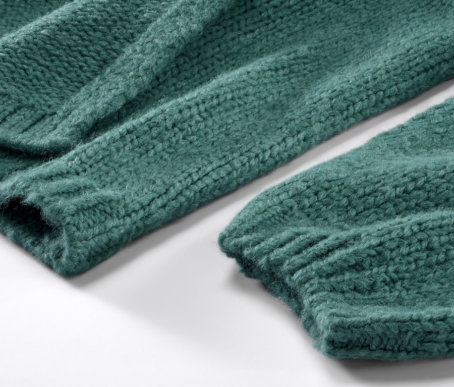 Detail zeleného otvoreného kardigánu z hrubej pleteniny.