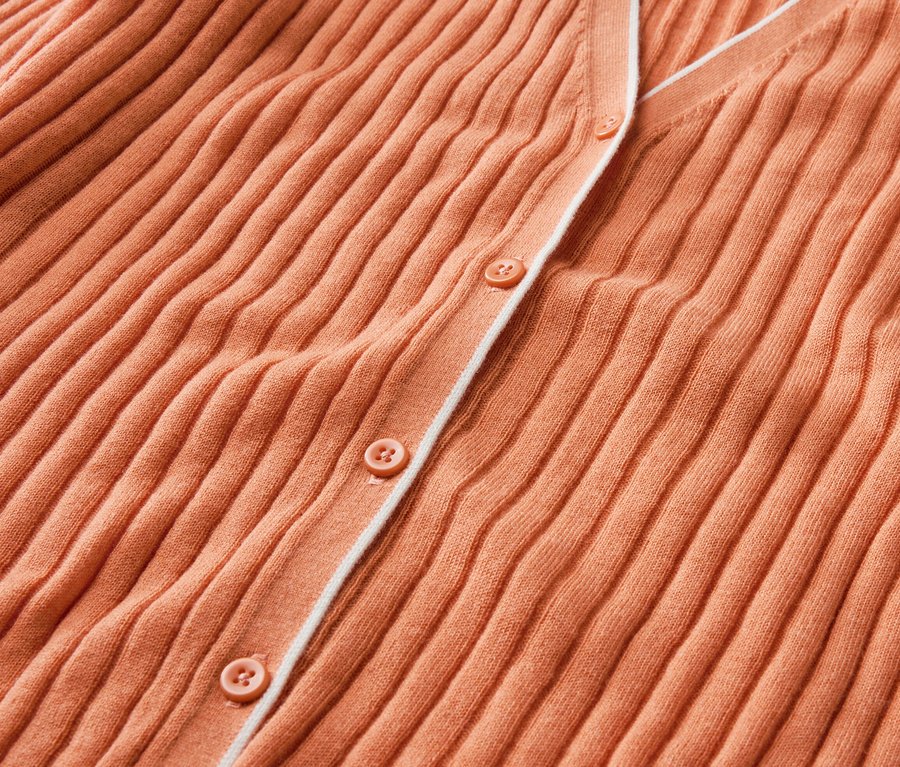 Detailný záber na oranžový kardigán s gombíkmi a hodvábom.