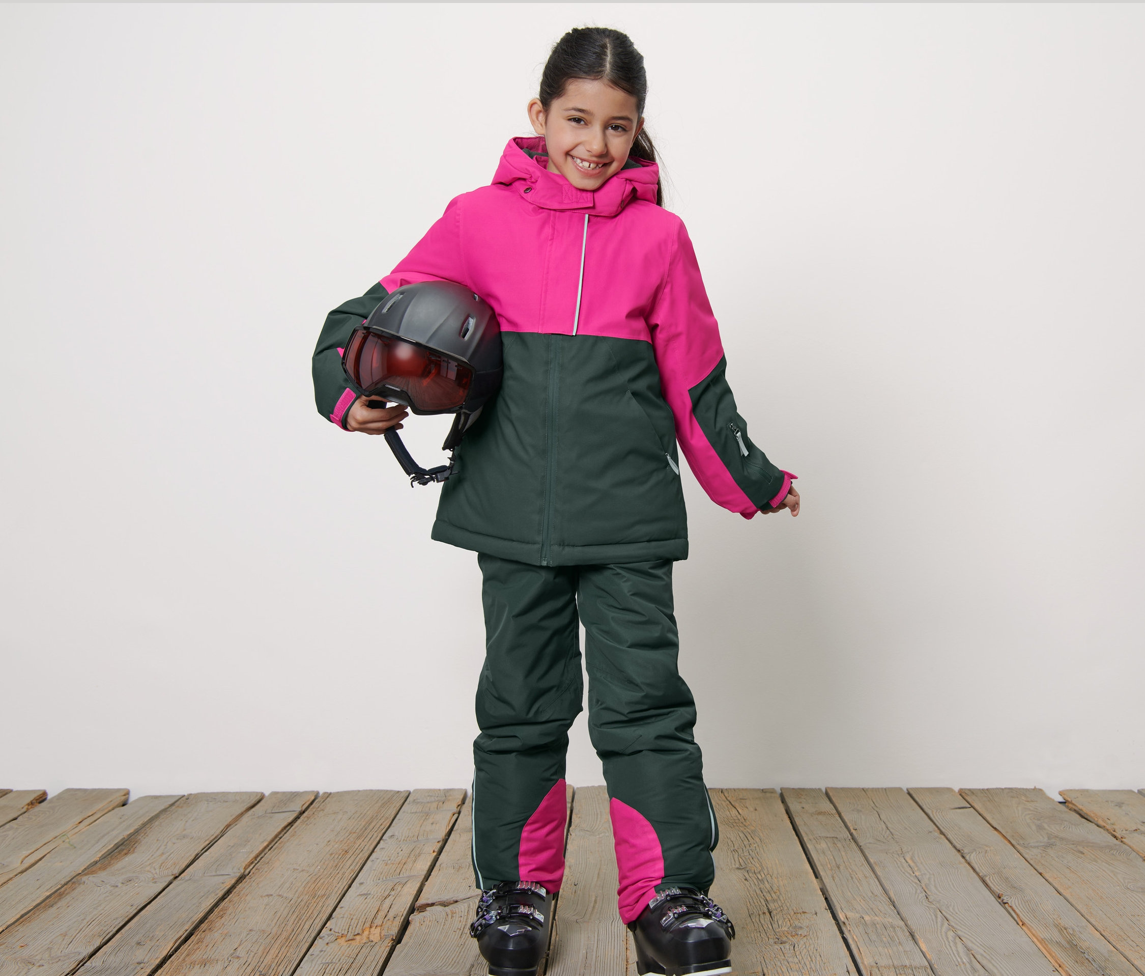 Usmievajúce sa dievča v detskej lyžiarskej bunde drží helmu.