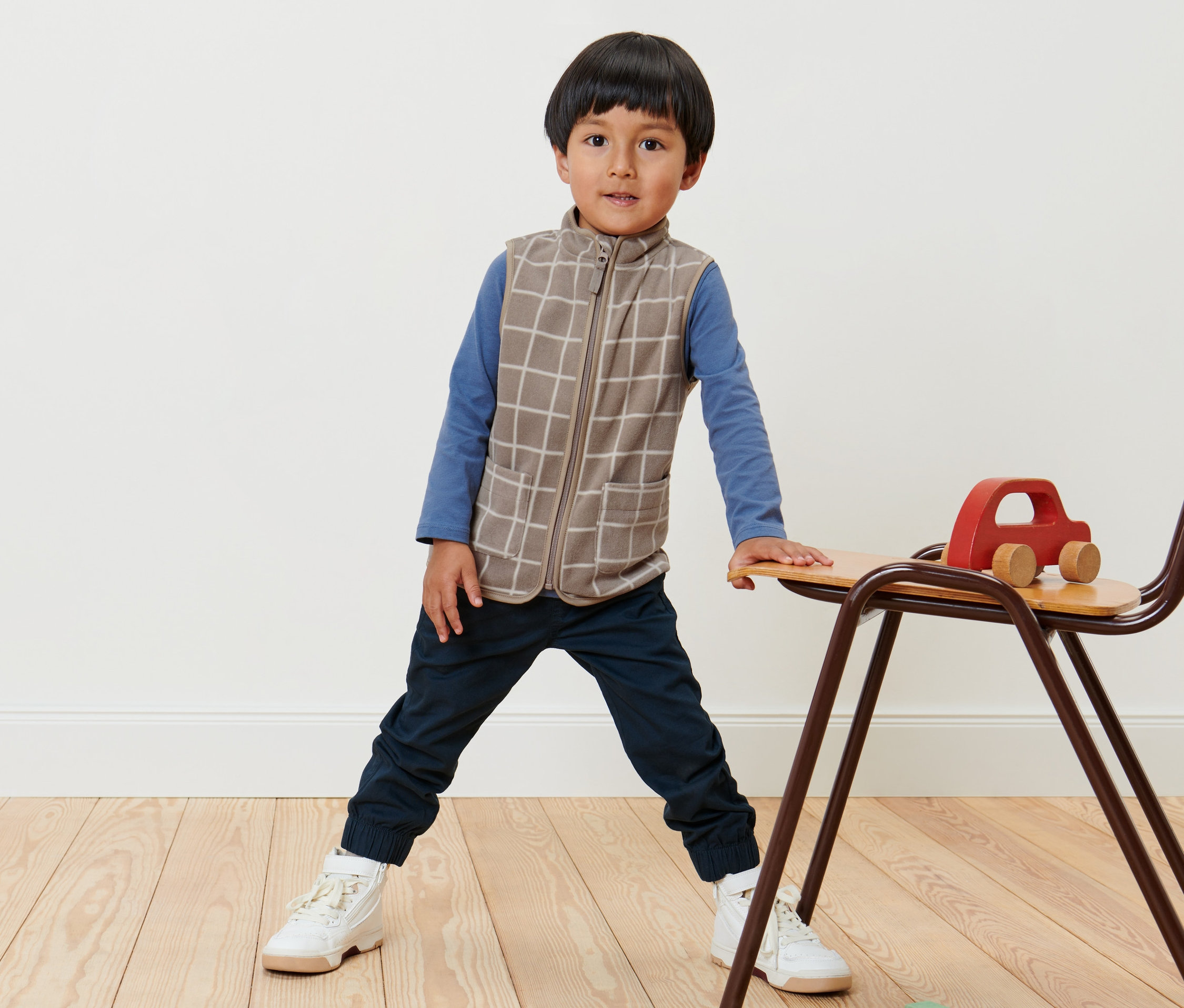 Chlapec stojí a má na sebe detskú flísovú vestu s károvaným vzorom.