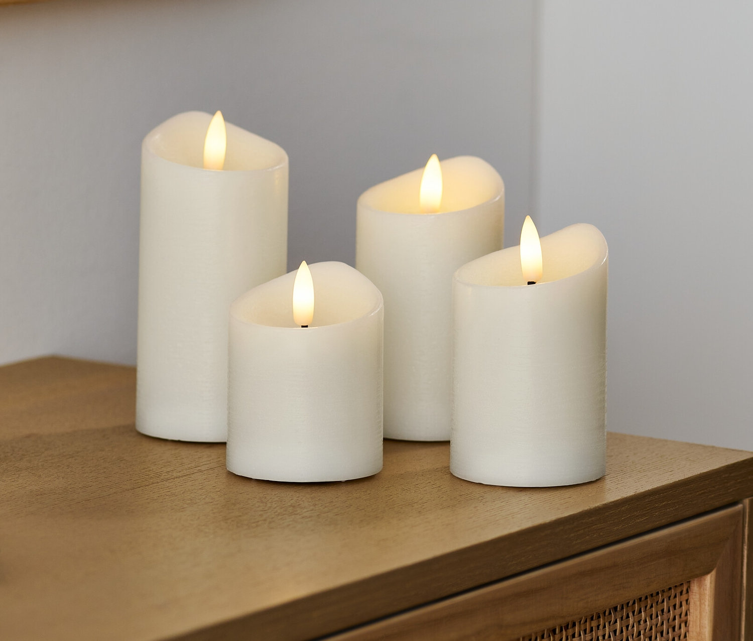 Štyri krémové LED sviečky z pravého vosku stoja na drevenej komode.