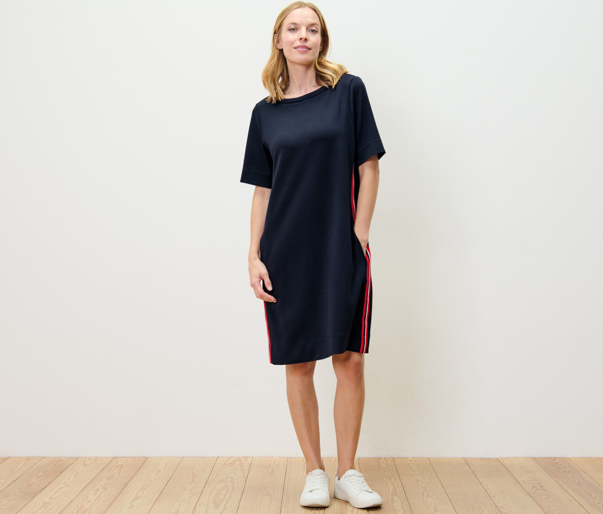 Žena stojí a má na sebe šaty z teplákoviny s lampasovými prúžkami.