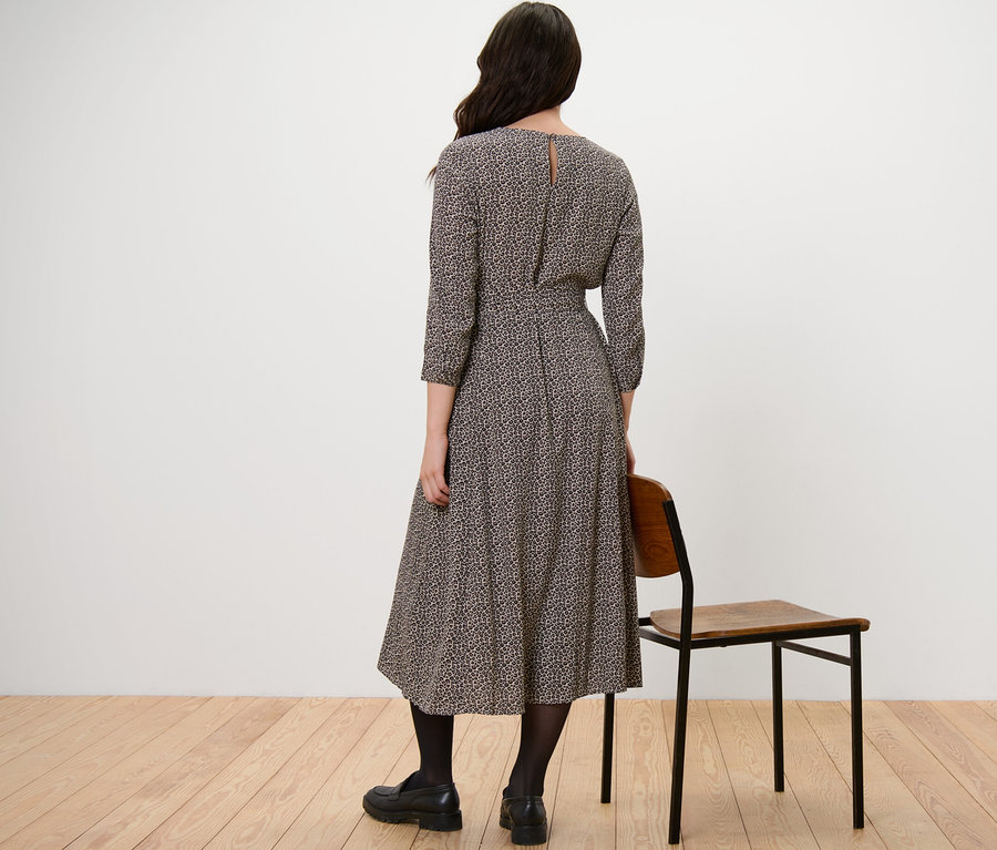 Žena stojí chrbtom k fotoaparátu a má na sebe tkané šaty s potlačou.