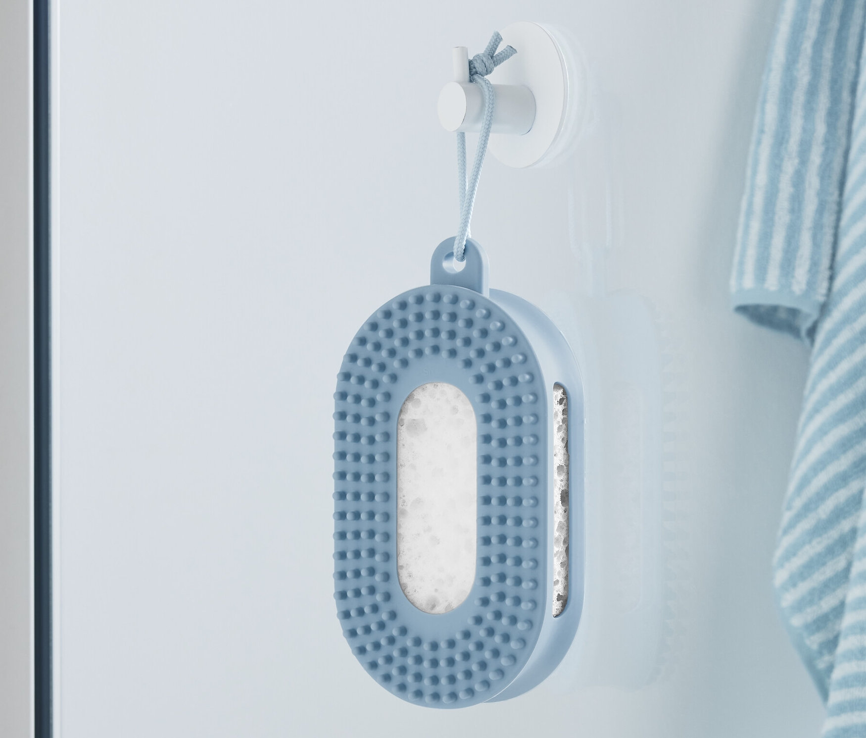 Modrá sprchová špongia visí na stene vedľa pruhovaného uteráka.