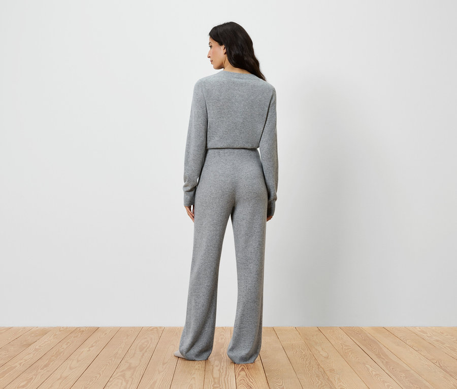 Žena stojí chrbtom k fotoaparátu a má na sebe sivý pletený top s dlhým rukávom a široké nohavice.