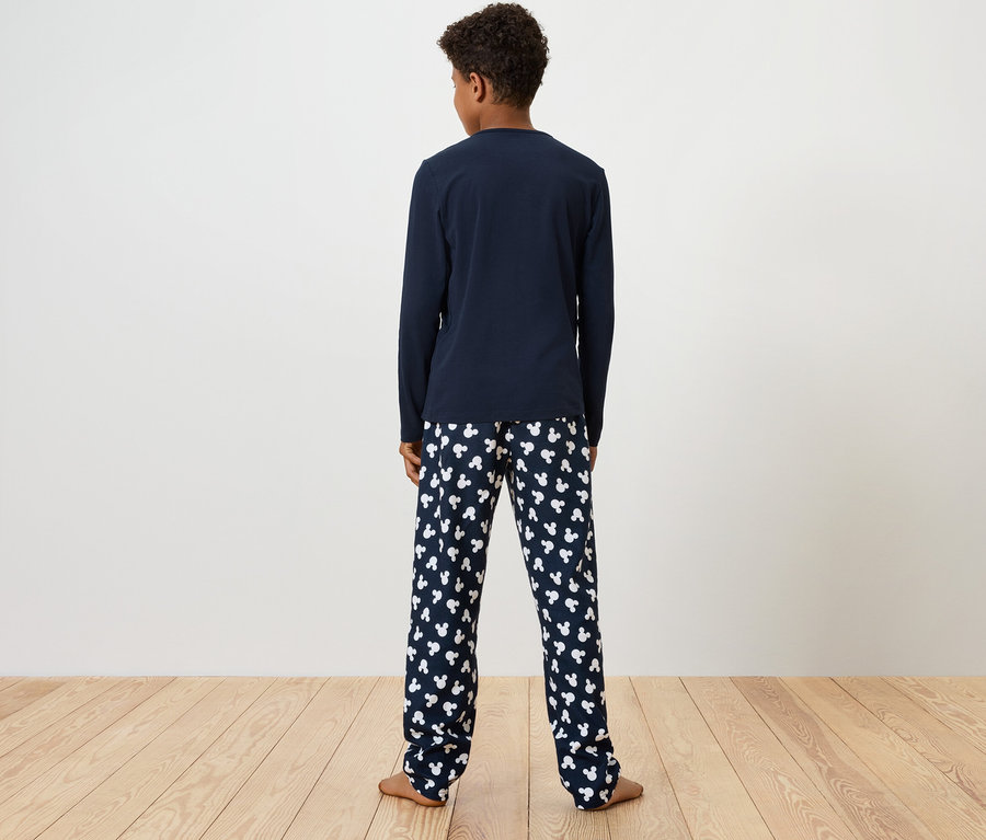 Chlapec stojí chrbtom k fotoaparátu, má na sebe modré pyžamové tričko s dlhým rukávom a pyžamové nohavice s potlačou bielych medvedíkov.