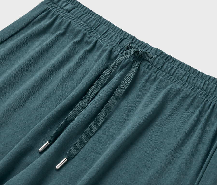 Detailný záber na elastický pás a sťahovaciu šnúrku zelenomodrých teplákov.
