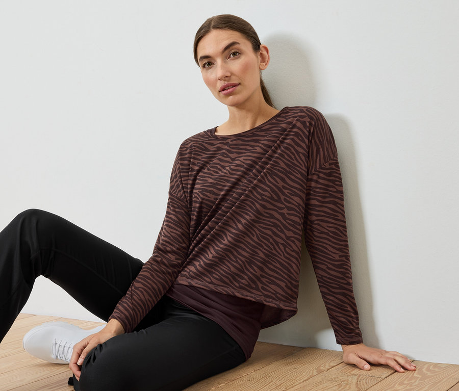 Žena sedí na podlahe v hnedo-čiernom zebrovanom tope a čiernych nohaviciach.