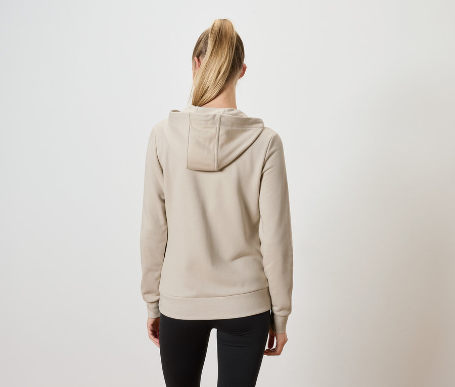 Zozadu je vidieť žena s blond vlasmi stiahnutými do copu, ktorá má na sebe béžovú mikinu s kapucňou a čierne nohavice.