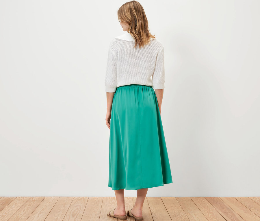 Žena zozadu stojí a má na sebe saténovú sukňu.