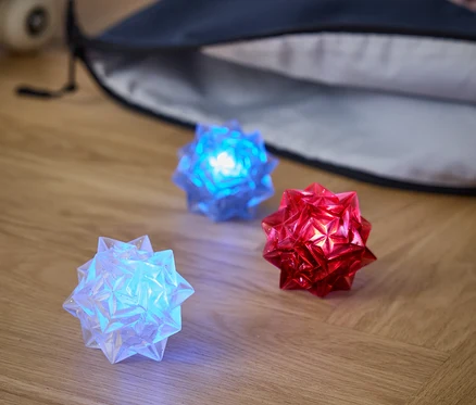 Na drevenej podlahe ležia tri svetelné gule: biela, modrá a červená. Za nimi je batoh a skateboard.