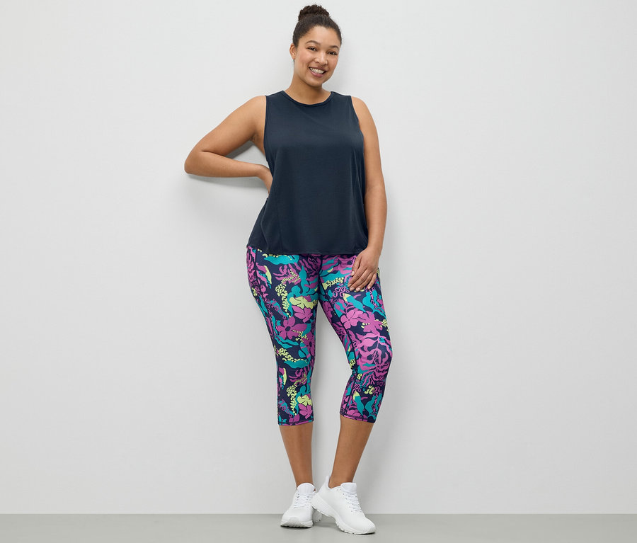 Žena pózuje v tmavomodrom športovom tope a v 3/4 športových legínsach s celoplošnou potlačou.