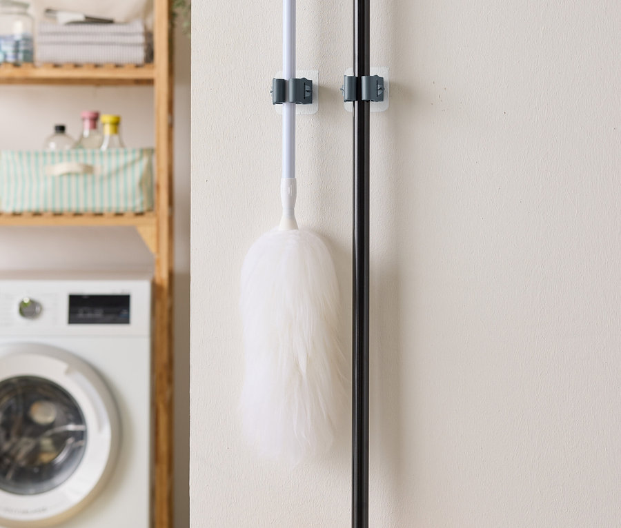 Na stene visí prachovka a metla, v pozadí je práčka a regál.