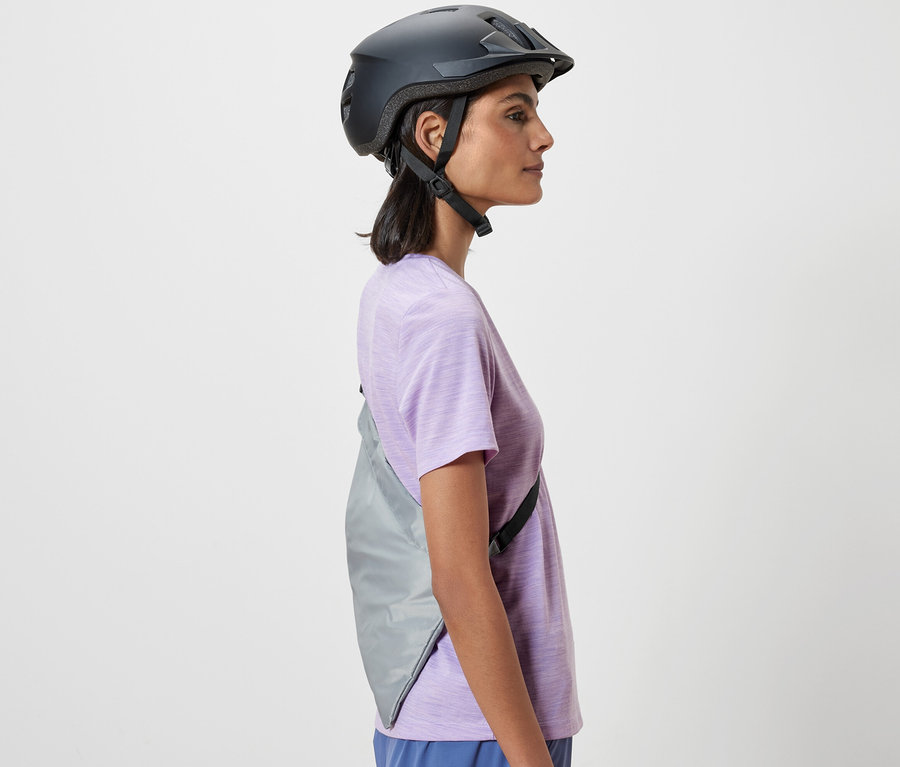 Bočný pohľad na ženu s cyklistickou helmou. Cez rameno má prehodenú nákupnú tašku na bicykel.