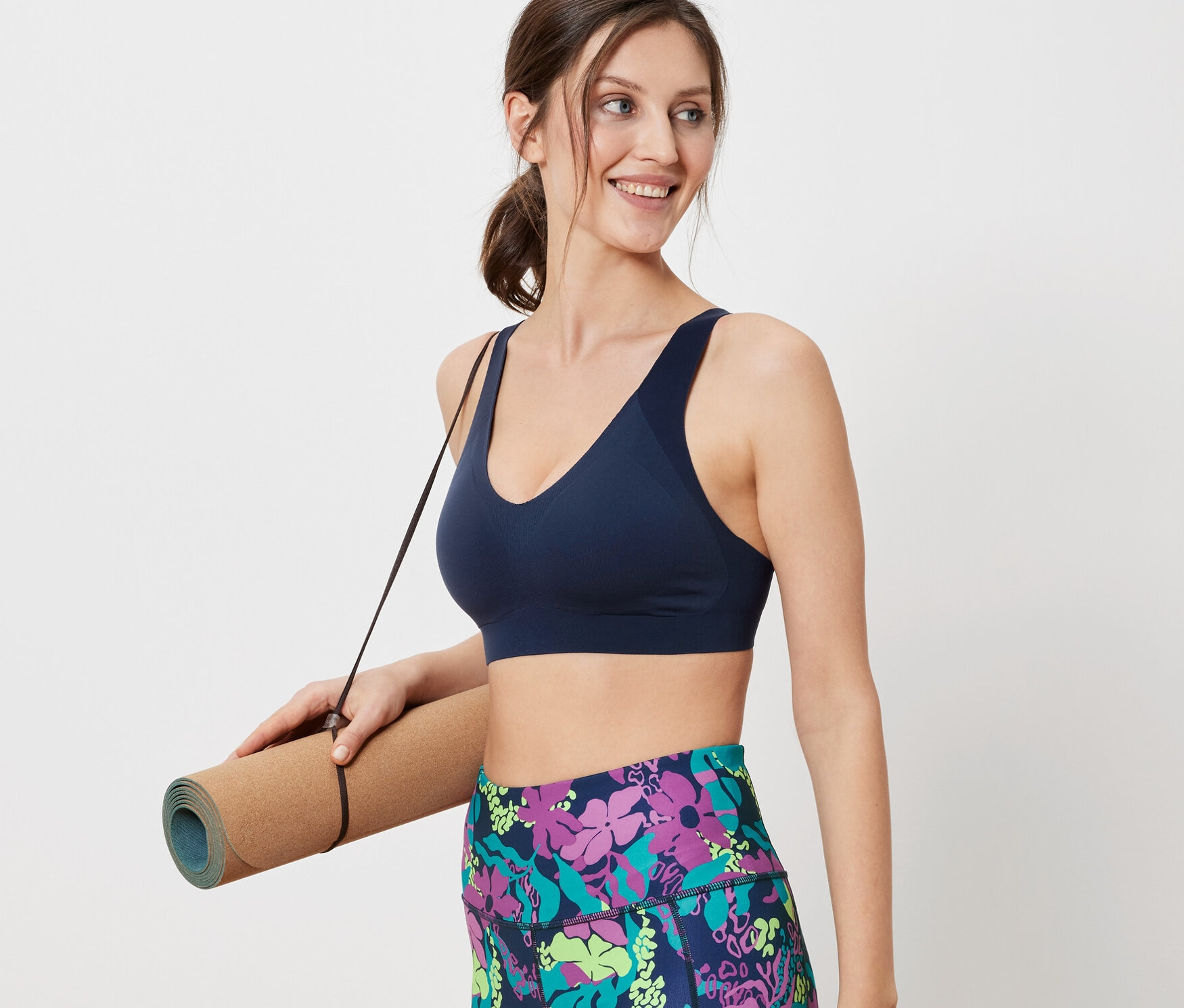 Žena drží podložku na cvičenie a má na sebe športovú podprsenku.