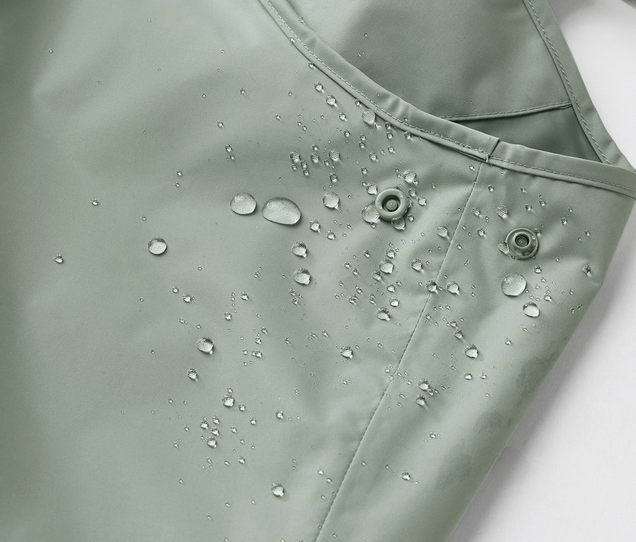 Detailný záber na vodeodolnú, svetlozelenú látku s kvapkami vody a dvoma patentkami.