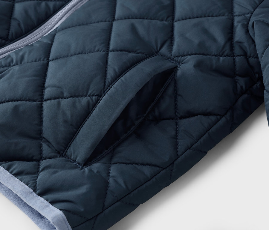 Detailný záber na tmavomodrú prešívanú bundu s vreckom.