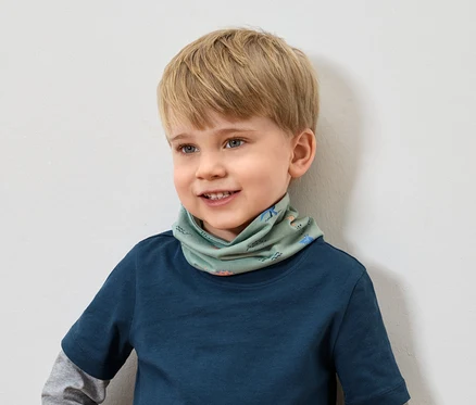 Usmievavý chlapec s blond vlasmi v modrom tričku má na sebe zelený šál so zvieracím vzorom.