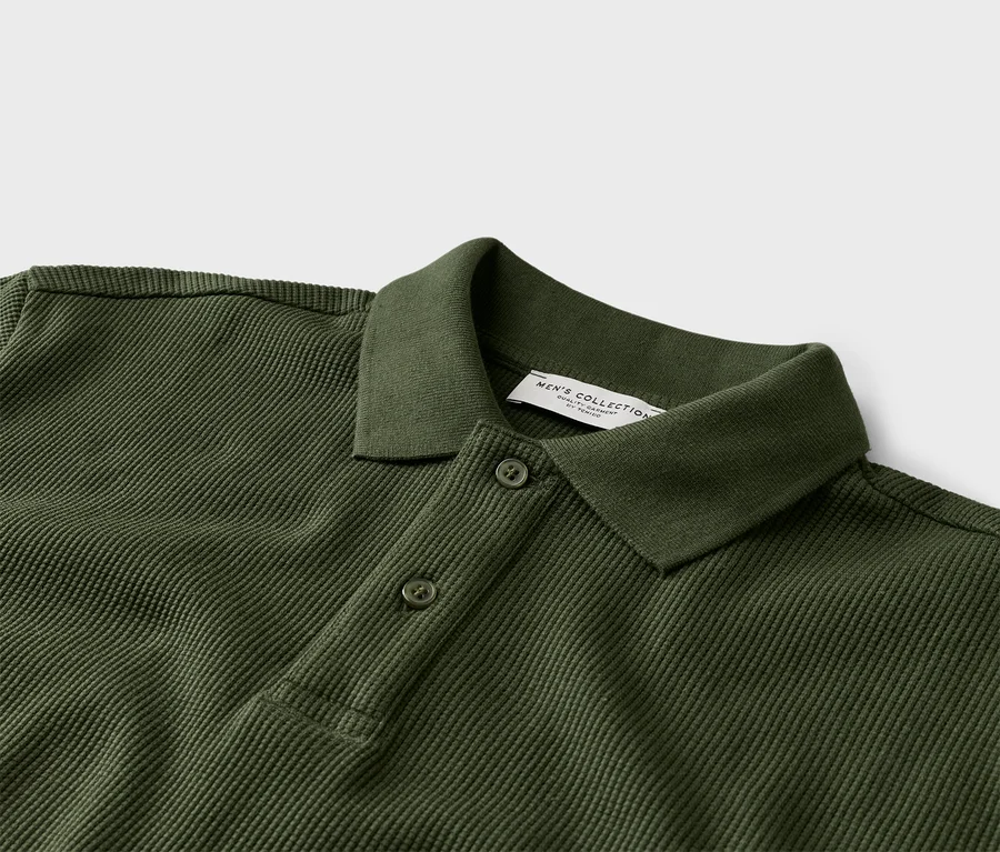 Detailný záber na olivovo zelené polo tričko s dvoma gombíkmi a golierom.