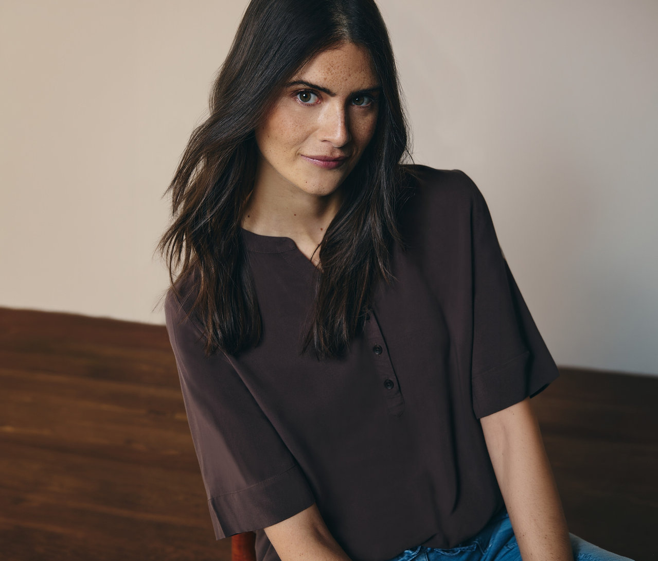 Žena má na sebe hnedú tunikovú blúzku CECIL a džínsy.