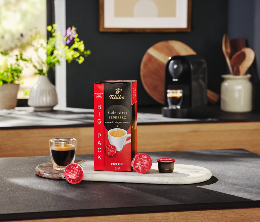 Na stole stojí balenie kapsúl Cafissimo Espresso, sklenica s espressom a kávovar.