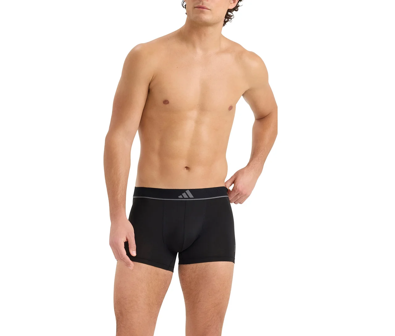 Muž bez trička v čiernych boxerkách so sivým pásom s logom troch pruhov. Jeho pravá ruka je na páse.