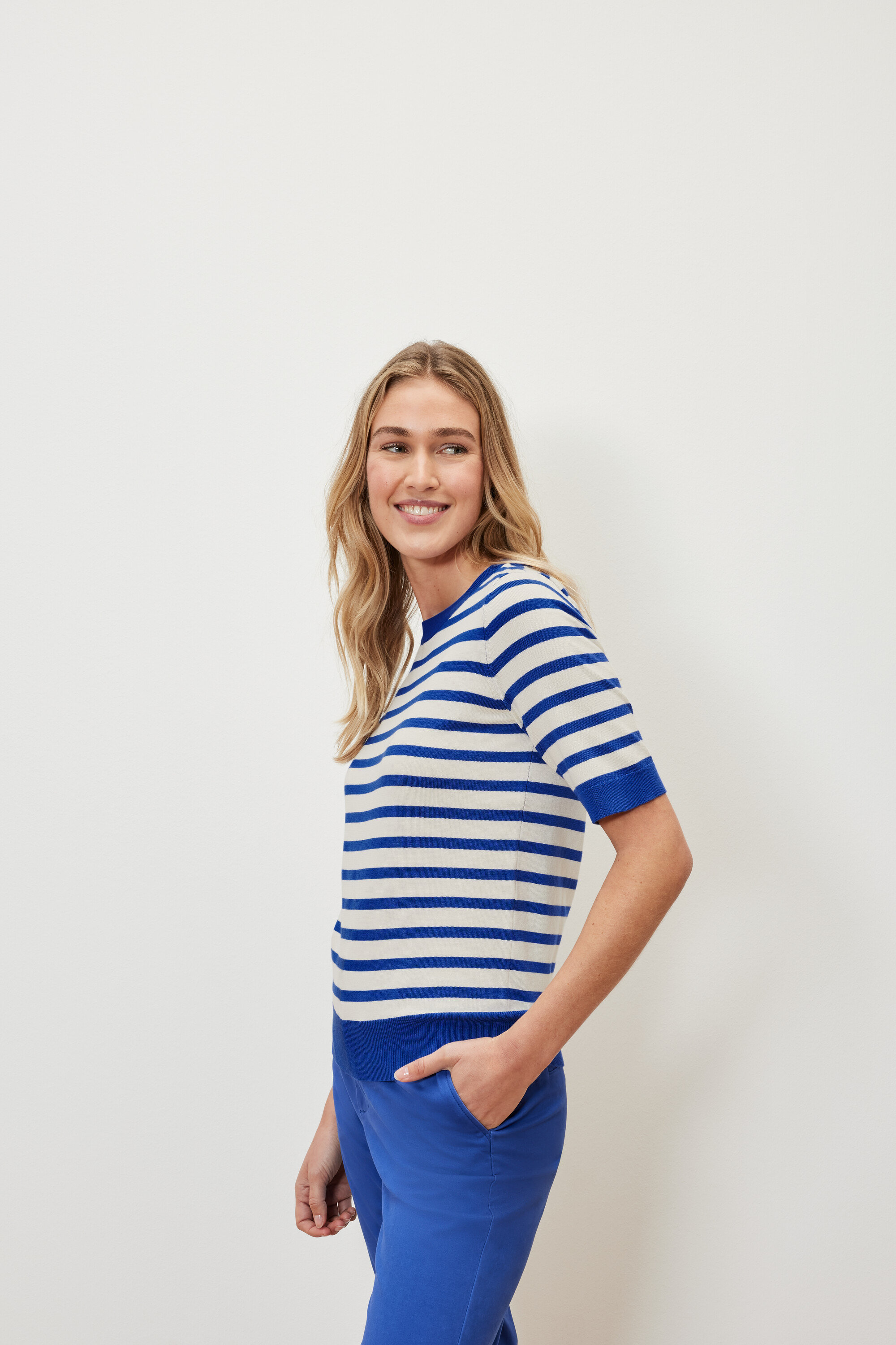 Žena má na sebe pruhovaný pulóver z jemného úpletu a modré nohavice.