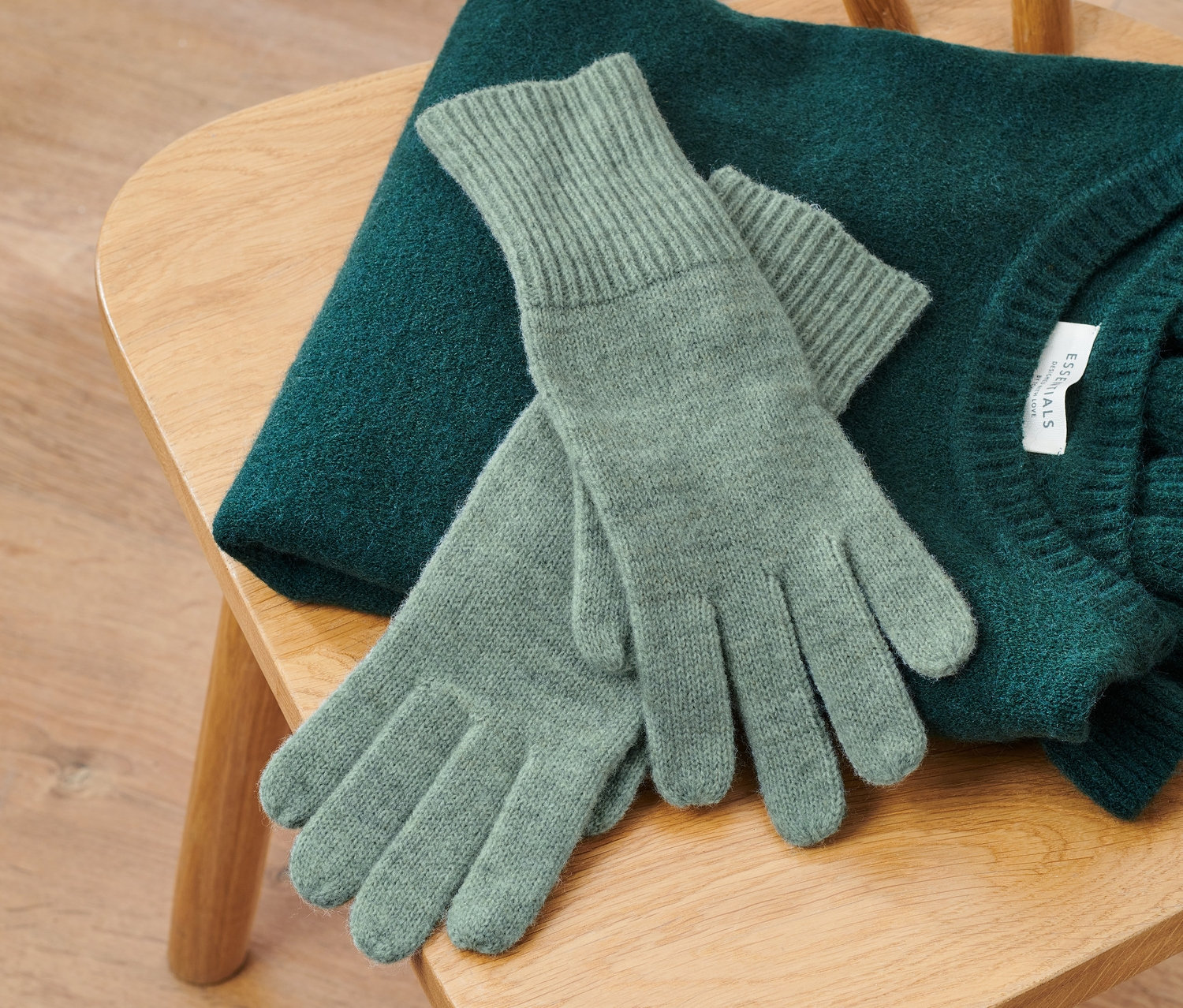 Na drevenej stoličke leží zelený sveter a pletené rukavice s vlnou vo farbe šalvie.