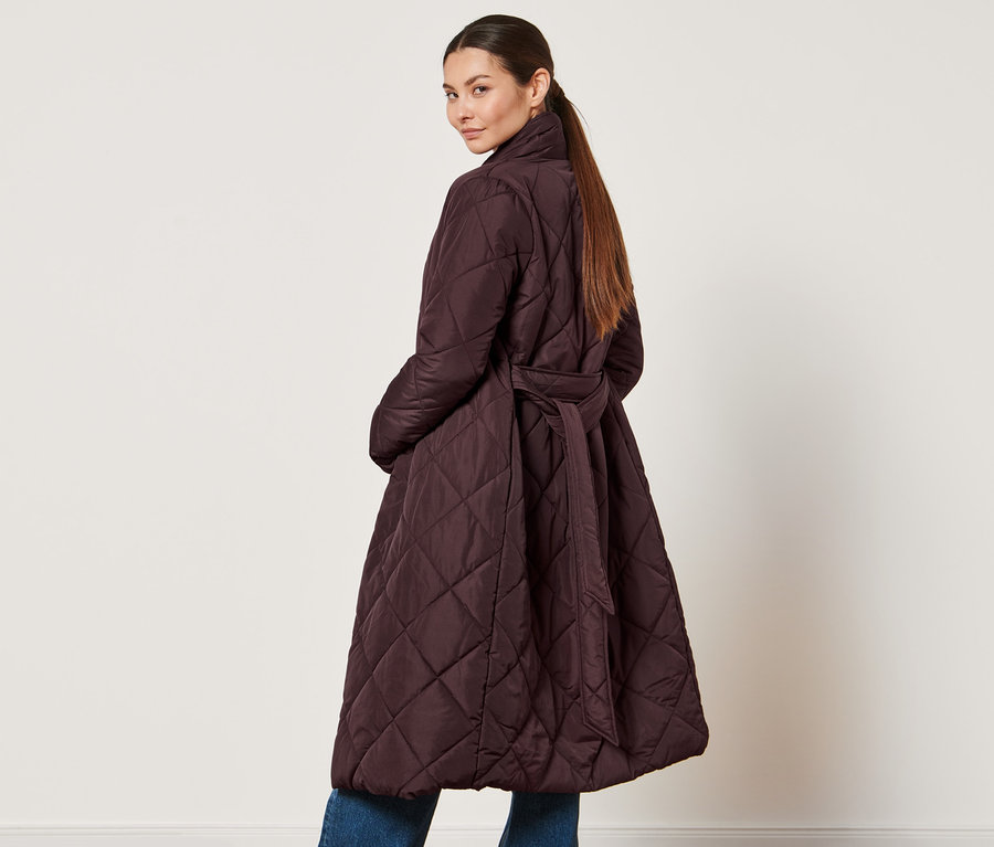 Žena sa pozerá cez plece a má na sebe prešívaný kabát.